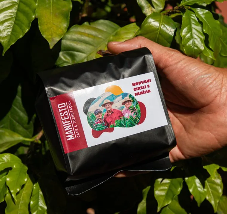 Pacote de café do Manifesto entre folhas de cafeeiro