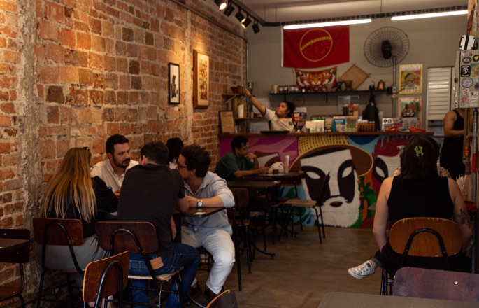 Salão da cafeteria com mesas e parede de tijolos